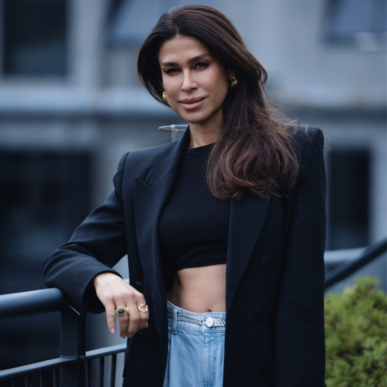 Woman wearing gold chunky hoop earrings, a black blazer, blue jeans and statement rings from RM Kandy